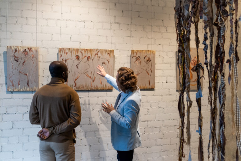 Contemporary artist presenting to young African male visitor one of his artworks hanging on wall in art gallery