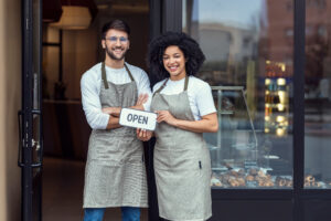 two people outside of a bakery holding an "open" sign