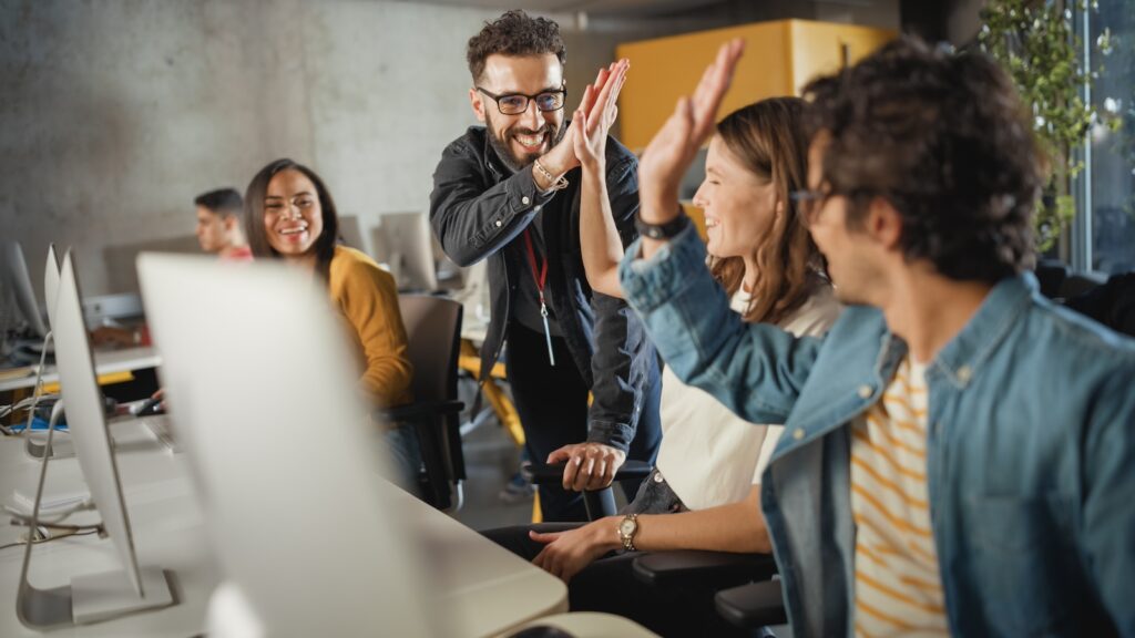 Group of computer users high-fiving each other at a desk station