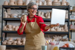 Woman pottery artist using laptop in art studio showing products