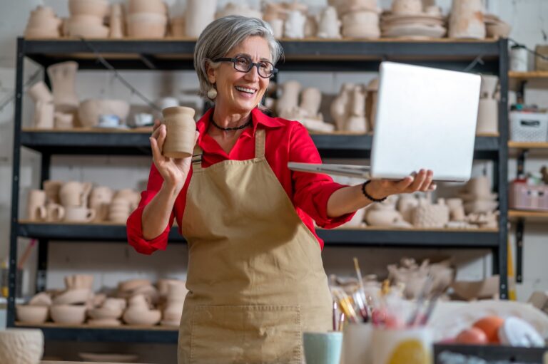 Woman pottery artist using laptop in art studio showing products