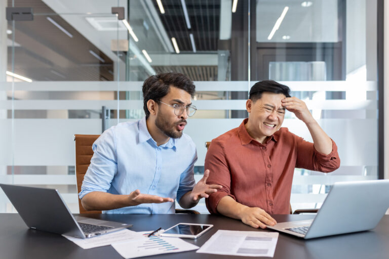 Two men sitting in front of a computer looking stressed